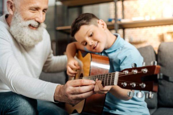 ensenando-gusto-feliz-anciano-ensenando-su-amado-nieto-tocar-guitarra-rasguear-acordes-mientras-sonrie-alegremente_259150-23061